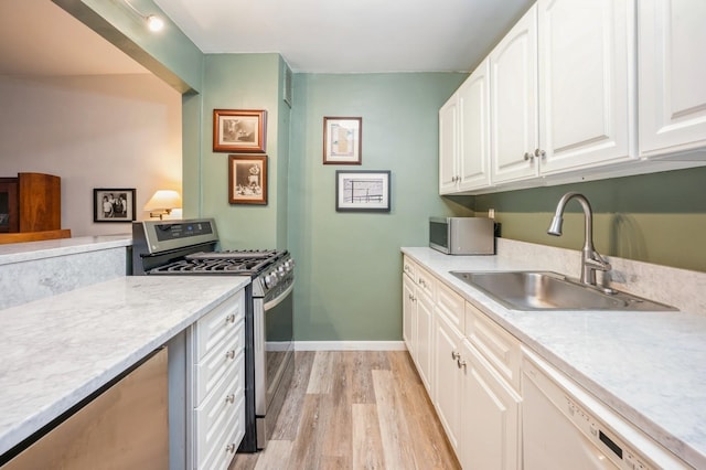 kitchen with stainless steel appliances, a sink, white cabinetry, and light wood-style floors