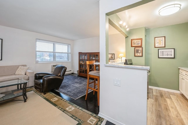 living room with light wood-type flooring, a baseboard radiator, a wall unit AC, and baseboards