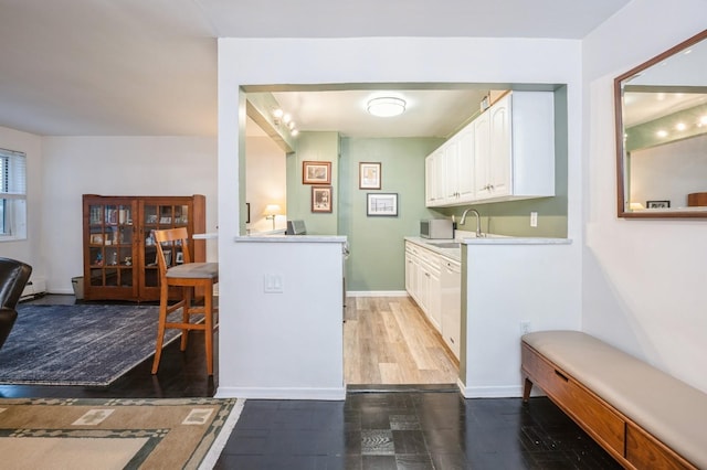 interior space featuring light countertops, white cabinetry, a sink, white dishwasher, and baseboards