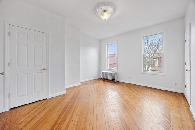 unfurnished room featuring baseboards, light wood finished floors, and radiator heating unit