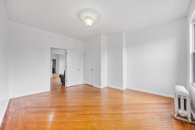 unfurnished room with light wood-type flooring, radiator, and baseboards
