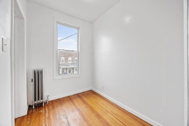 spare room featuring baseboards, light wood-style flooring, and radiator