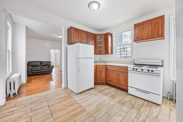 kitchen featuring radiator, white appliances, wood tiled floor, and brown cabinets