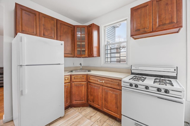 kitchen featuring white appliances, glass insert cabinets, brown cabinets, light countertops, and a sink