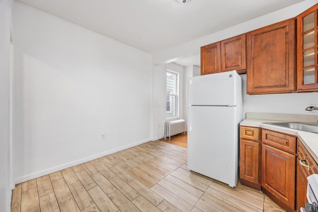 kitchen with light wood finished floors, light countertops, radiator heating unit, freestanding refrigerator, and a sink