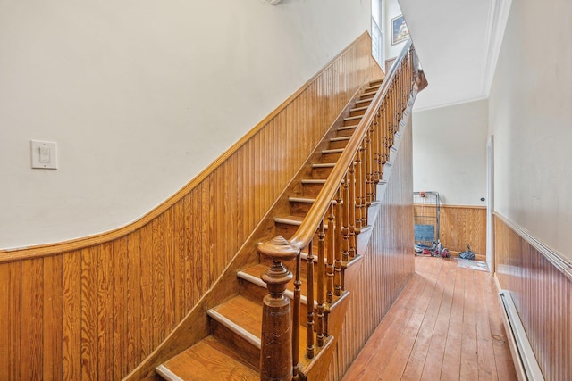 staircase with hardwood / wood-style flooring, wooden walls, baseboard heating, and wainscoting