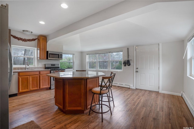 kitchen featuring brown cabinets, wood finished floors, baseboard heating, stainless steel appliances, and a sink