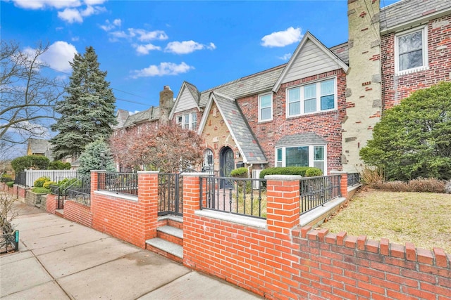 tudor home featuring a fenced front yard, a high end roof, brick siding, and a gate