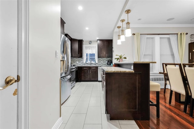 kitchen with dark brown cabinets, pendant lighting, a kitchen bar, decorative backsplash, and stainless steel appliances