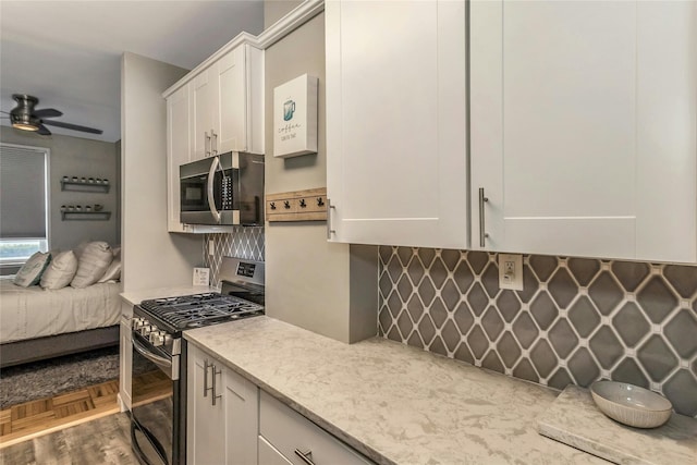 kitchen with open floor plan, light stone counters, appliances with stainless steel finishes, white cabinets, and a ceiling fan