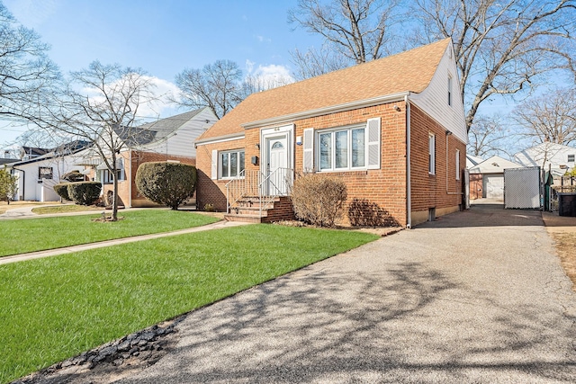 bungalow-style home featuring a front yard, an outdoor structure, a garage, aphalt driveway, and brick siding