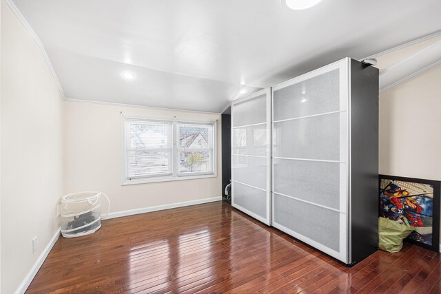 unfurnished bedroom featuring lofted ceiling, crown molding, baseboards, and wood-type flooring