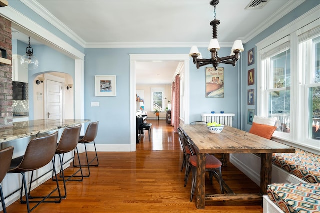 dining area with visible vents, baseboards, ornamental molding, wood finished floors, and arched walkways