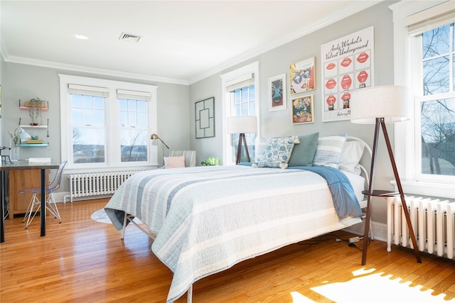 bedroom with radiator, wood finished floors, visible vents, and ornamental molding