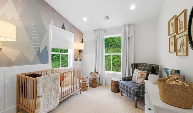 carpeted bedroom featuring a crib, multiple windows, visible vents, and wainscoting