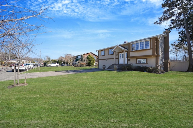 view of front of property with stucco siding, a front lawn, driveway, and fence