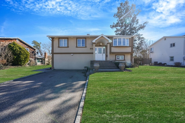 raised ranch with stucco siding, driveway, and a front lawn