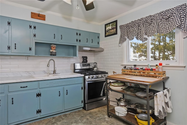 kitchen with stainless steel gas range, blue cabinetry, a sink, under cabinet range hood, and crown molding