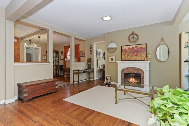 living area featuring a notable chandelier, baseboards, a lit fireplace, and wood finished floors