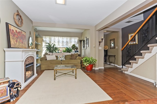 living area with dark wood finished floors, a glass covered fireplace, stairs, and baseboards