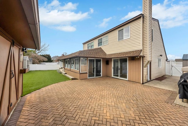 back of property with a fenced backyard, a sunroom, a lawn, a gate, and a patio area