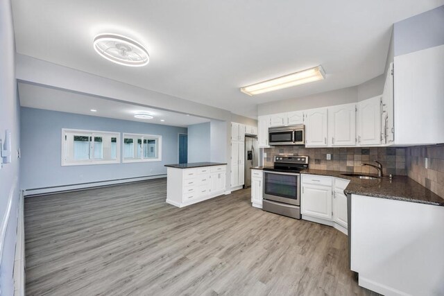 kitchen featuring tasteful backsplash, white cabinets, stainless steel appliances, a baseboard heating unit, and a sink