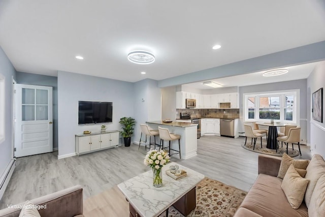 living area featuring a baseboard heating unit, light wood-type flooring, baseboards, and recessed lighting