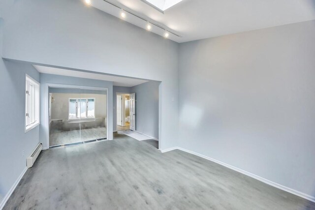 unfurnished room featuring a skylight, baseboards, baseboard heating, and wood finished floors