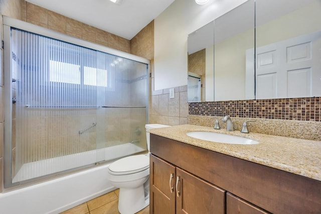 full bath with bath / shower combo with glass door, toilet, tile patterned floors, vanity, and tile walls