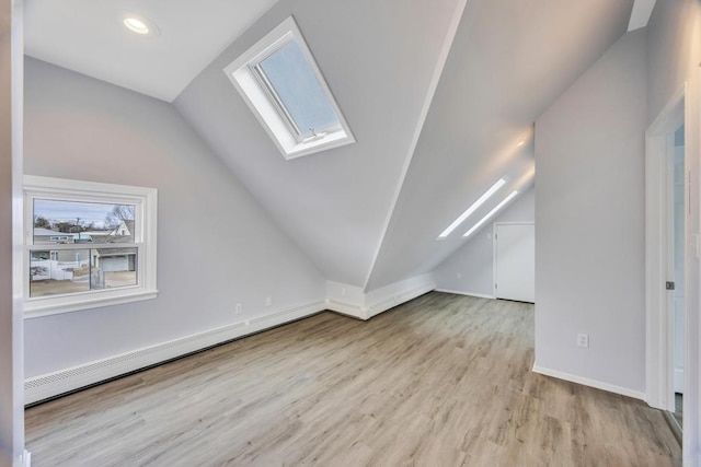 additional living space featuring a baseboard heating unit, vaulted ceiling with skylight, wood finished floors, and baseboards