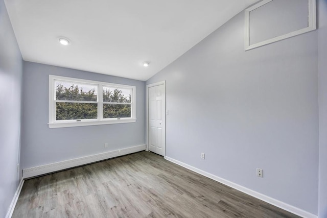 empty room with baseboards, vaulted ceiling, baseboard heating, and wood finished floors