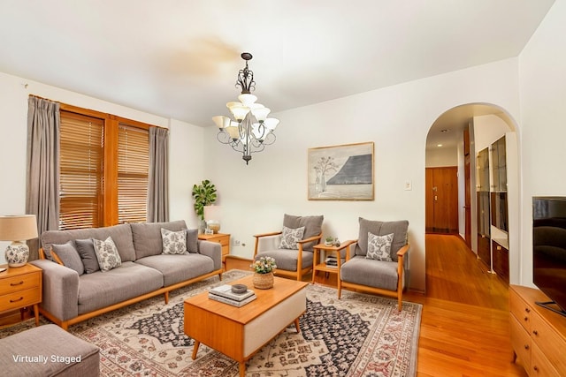 living area with light wood-style floors, arched walkways, and a notable chandelier