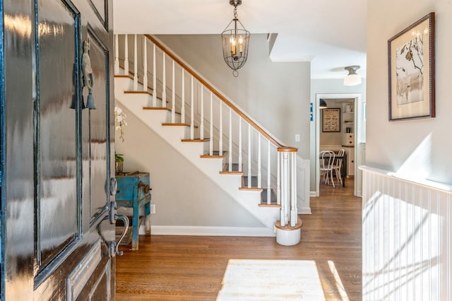 foyer entrance with a chandelier, baseboards, stairs, and wood finished floors