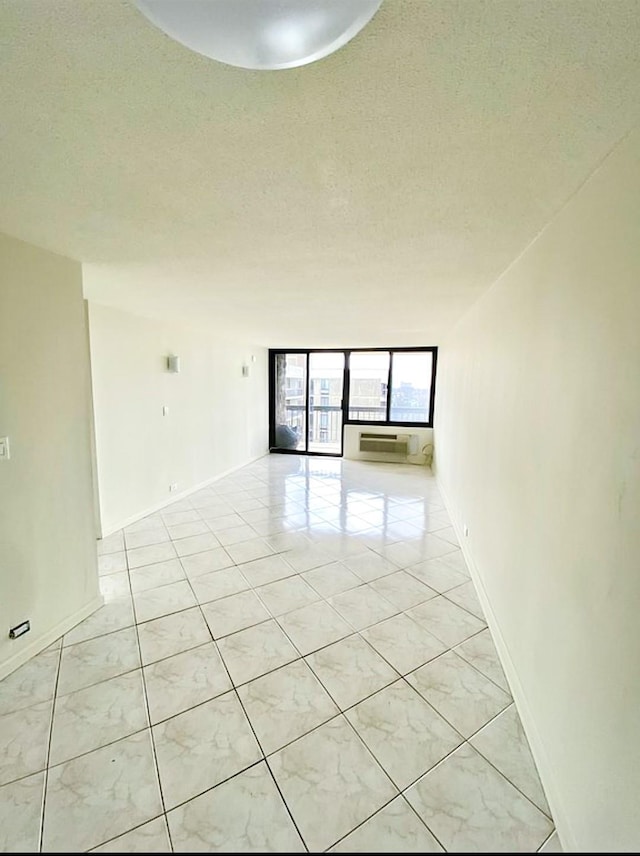 empty room with a textured ceiling, light tile patterned floors, and baseboards