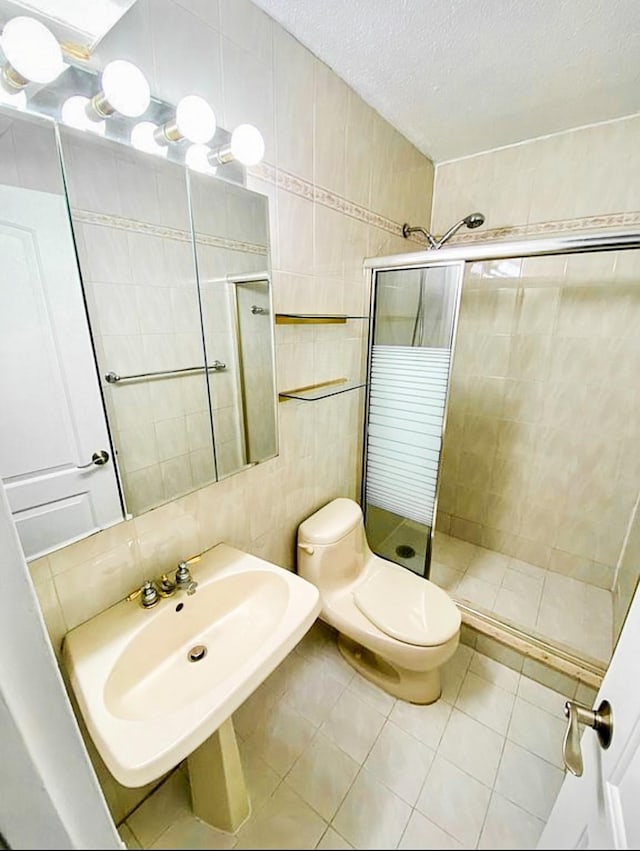 full bath with toilet, a sink, tile walls, a shower stall, and tile patterned floors