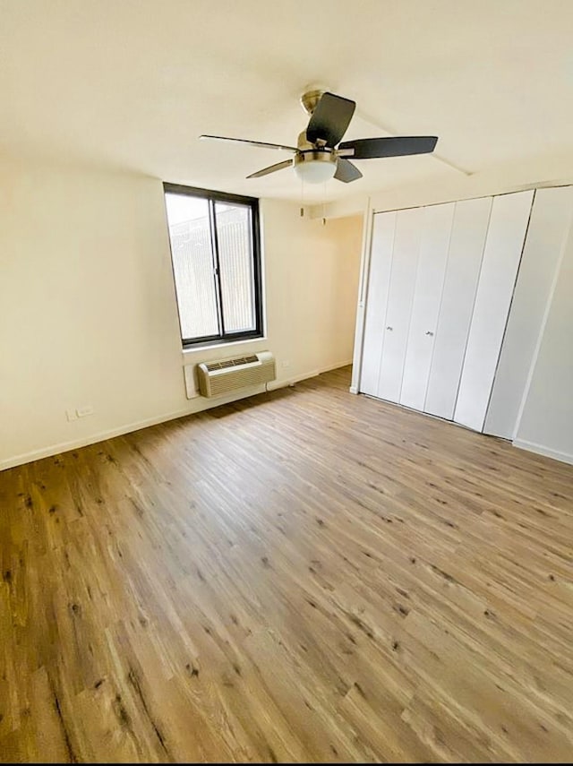 unfurnished bedroom with a wall mounted AC, wood finished floors, and a ceiling fan