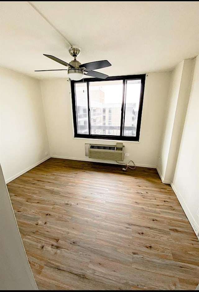 empty room with a ceiling fan, a wall unit AC, baseboards, and wood finished floors