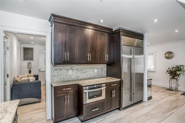 kitchen featuring stainless steel appliances, dark brown cabinetry, decorative backsplash, and light stone countertops