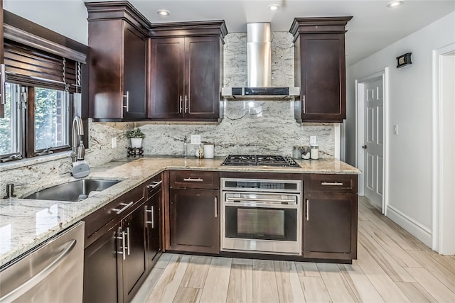 kitchen with decorative backsplash, appliances with stainless steel finishes, a sink, wall chimney range hood, and light stone countertops