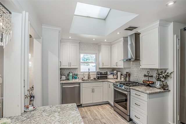 kitchen with a sink, visible vents, white cabinets, appliances with stainless steel finishes, and wall chimney exhaust hood