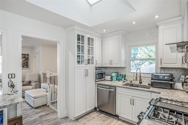 kitchen featuring decorative backsplash, appliances with stainless steel finishes, light wood-type flooring, white cabinetry, and a sink