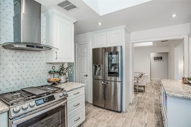 kitchen with stainless steel appliances, wall chimney exhaust hood, visible vents, and white cabinetry