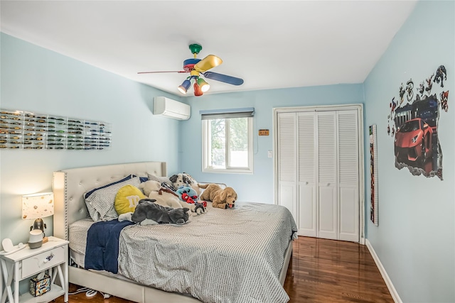 bedroom with a closet, an AC wall unit, ceiling fan, wood finished floors, and baseboards