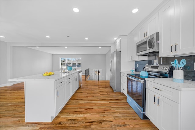 kitchen featuring appliances with stainless steel finishes, light wood-type flooring, white cabinetry, and a kitchen island with sink