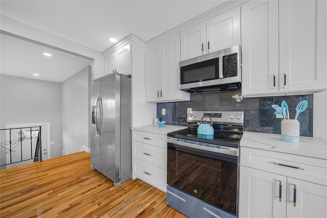 kitchen featuring tasteful backsplash, white cabinets, light stone countertops, stainless steel appliances, and light wood-style floors