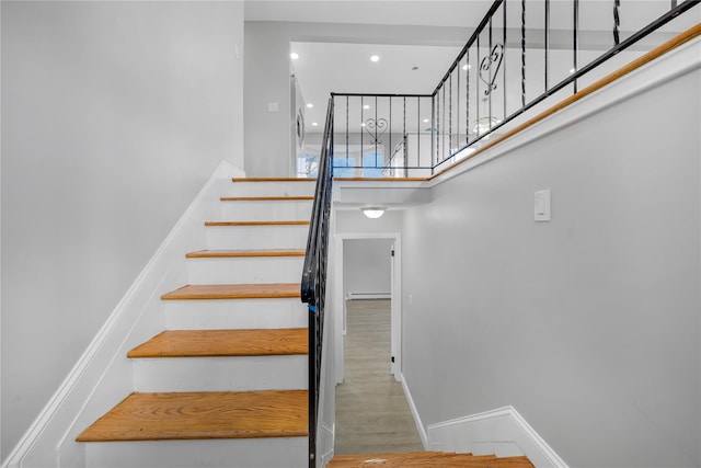 staircase featuring a towering ceiling, baseboards, wood finished floors, and recessed lighting