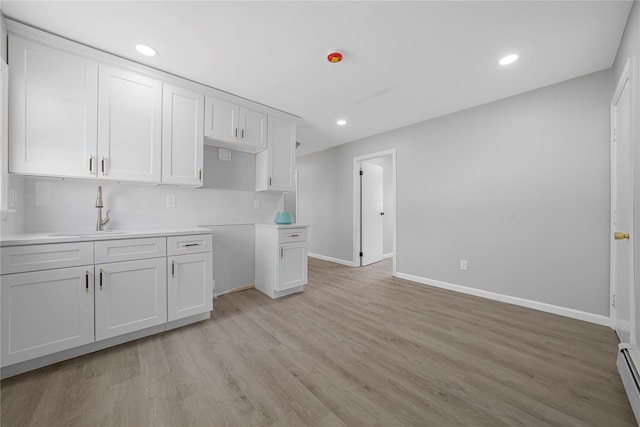 kitchen with baseboard heating, light wood-type flooring, white cabinetry, a sink, and recessed lighting