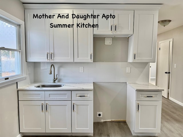 kitchen featuring light stone counters, light wood-style flooring, a sink, baseboards, and white cabinets