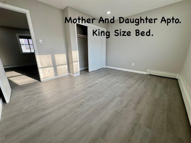 unfurnished bedroom featuring a baseboard heating unit, a closet, baseboards, and wood finished floors