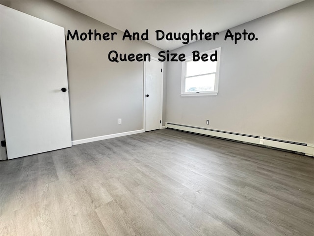 empty room featuring a baseboard heating unit and wood finished floors